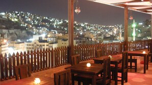 An outdoor dining area with tables and chairs, a wooden fence, and a cityscape view in the background. - Arab Tower Hotel (Amman)