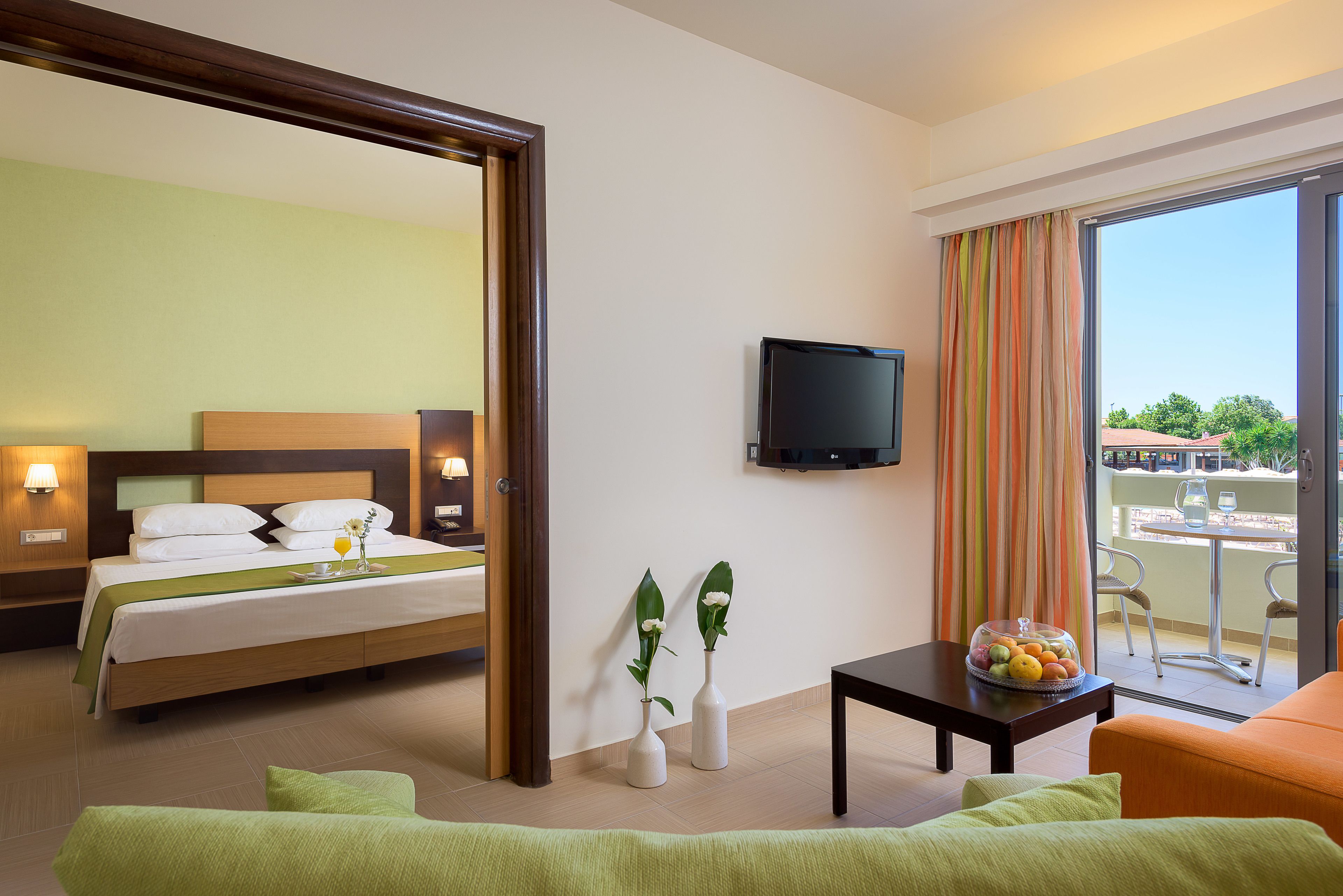 Habitación de hotel con cama, televisión, balcón con mesa y sillas, y vista al exterior.