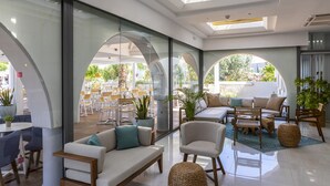 A modern interior with a glass wall, a sofa, a chair, and a dining area with tables and chairs. - Leonardo Kolymbia Resort - All Inclusive (Rhodes)
