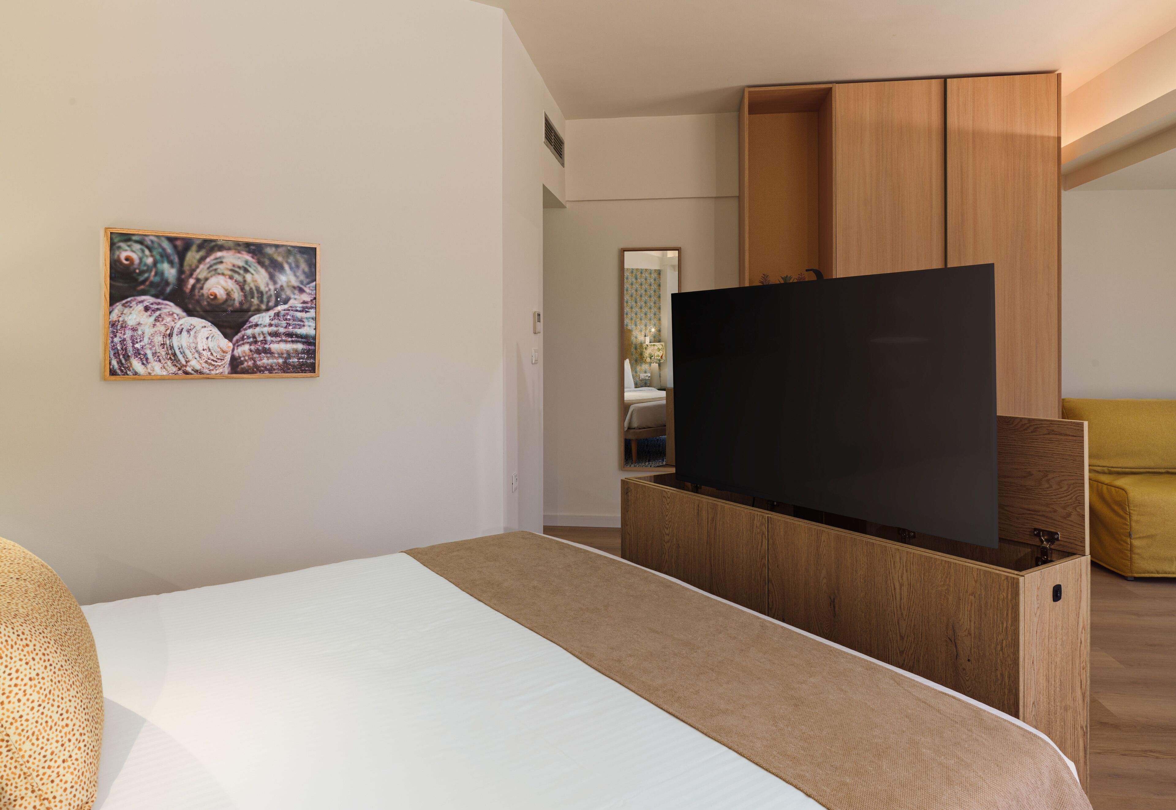 Una habitación de hotel moderna con una cama, un televisor de pantalla plana, un armario de madera y un cuadro en la pared.