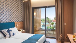 A hotel room with a bed, a desk with a chair, a view of a pool, and a balcony with curtains. - Leonardo Kolymbia Resort - All Inclusive (Rhodes)