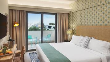Habitación de hotel con cama, escritorio con una botella y vasos, una silla y vista al exterior.