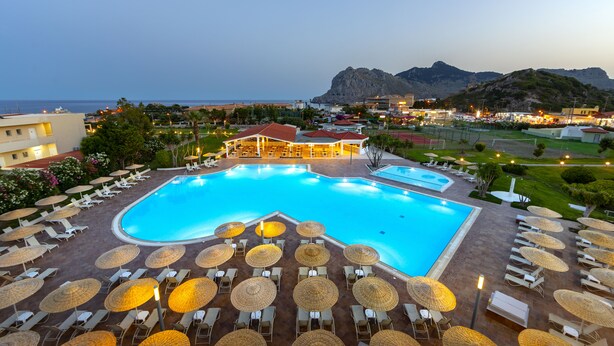 A large swimming pool with sun loungers and umbrellas, surrounded by buildings and a mountainous backdrop. - Leonardo Kolymbia Resort - All Inclusive (Rhodes)