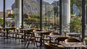 A restaurant with outdoor seating, large windows, and a view of mountains. - Leonardo Kolymbia Resort - All Inclusive (Rhodes)