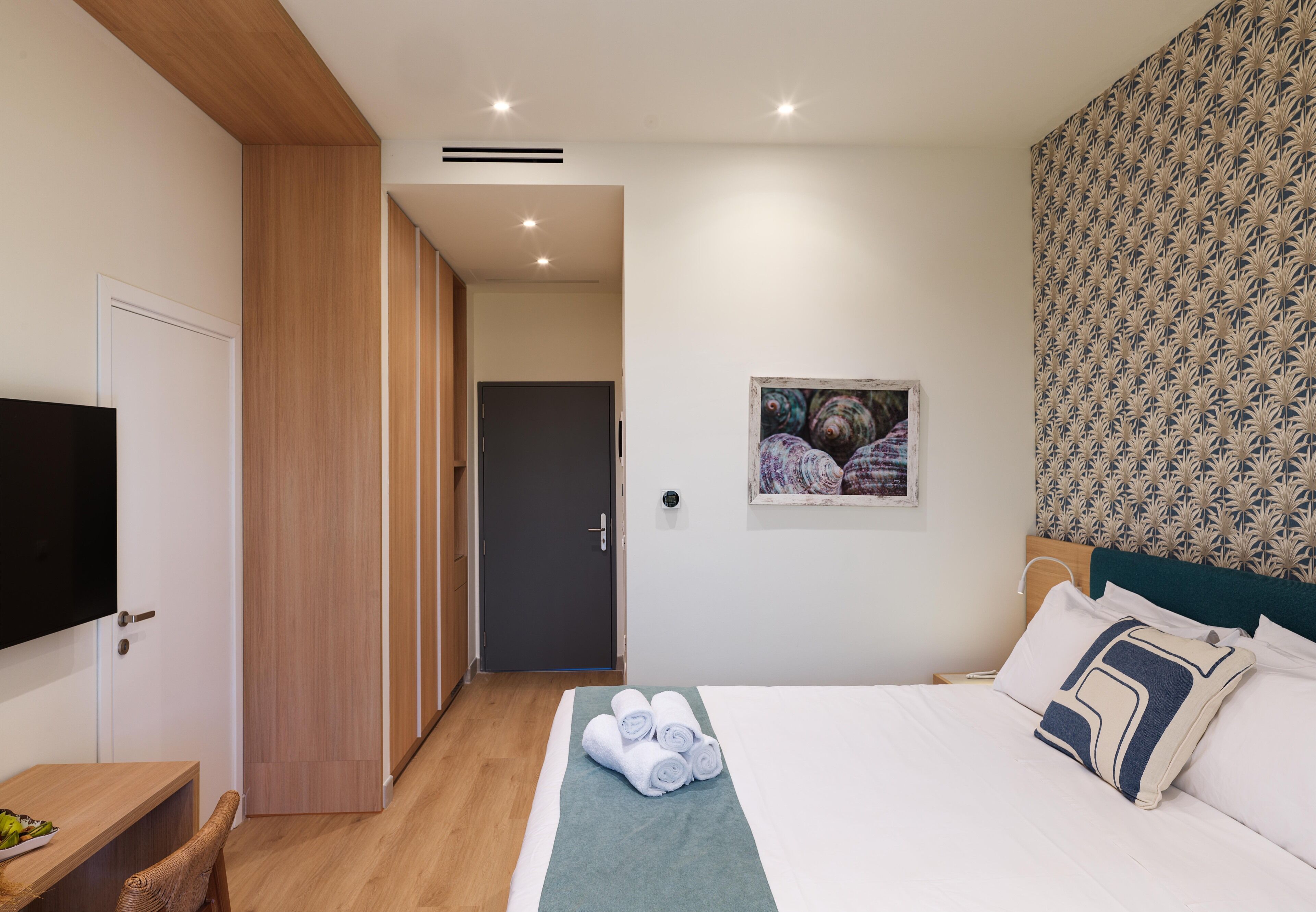 Een hotelkamer met een bed, een televisie, een houten garderobe en een deur naar een andere kamer.