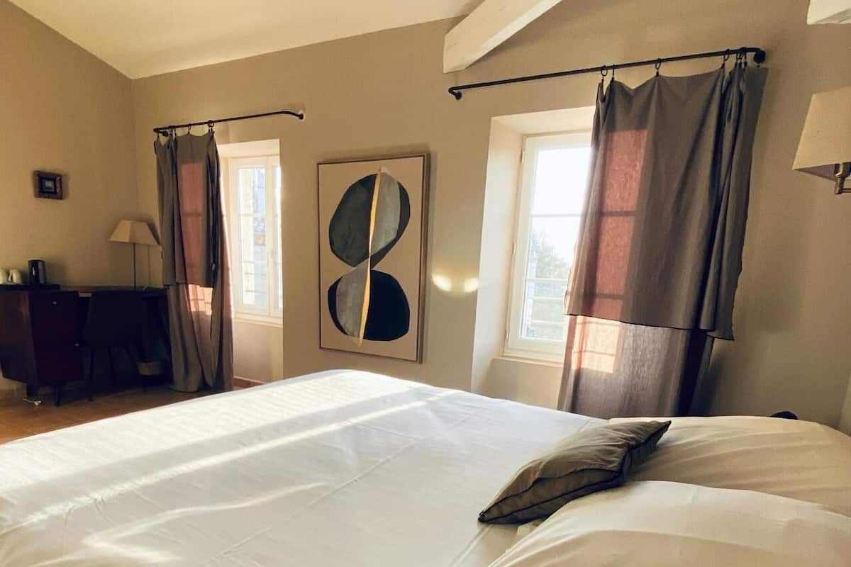 Une chambre d’hôtel avec un grand lit, un bureau avec une chaise et une fenêtre avec des rideaux.