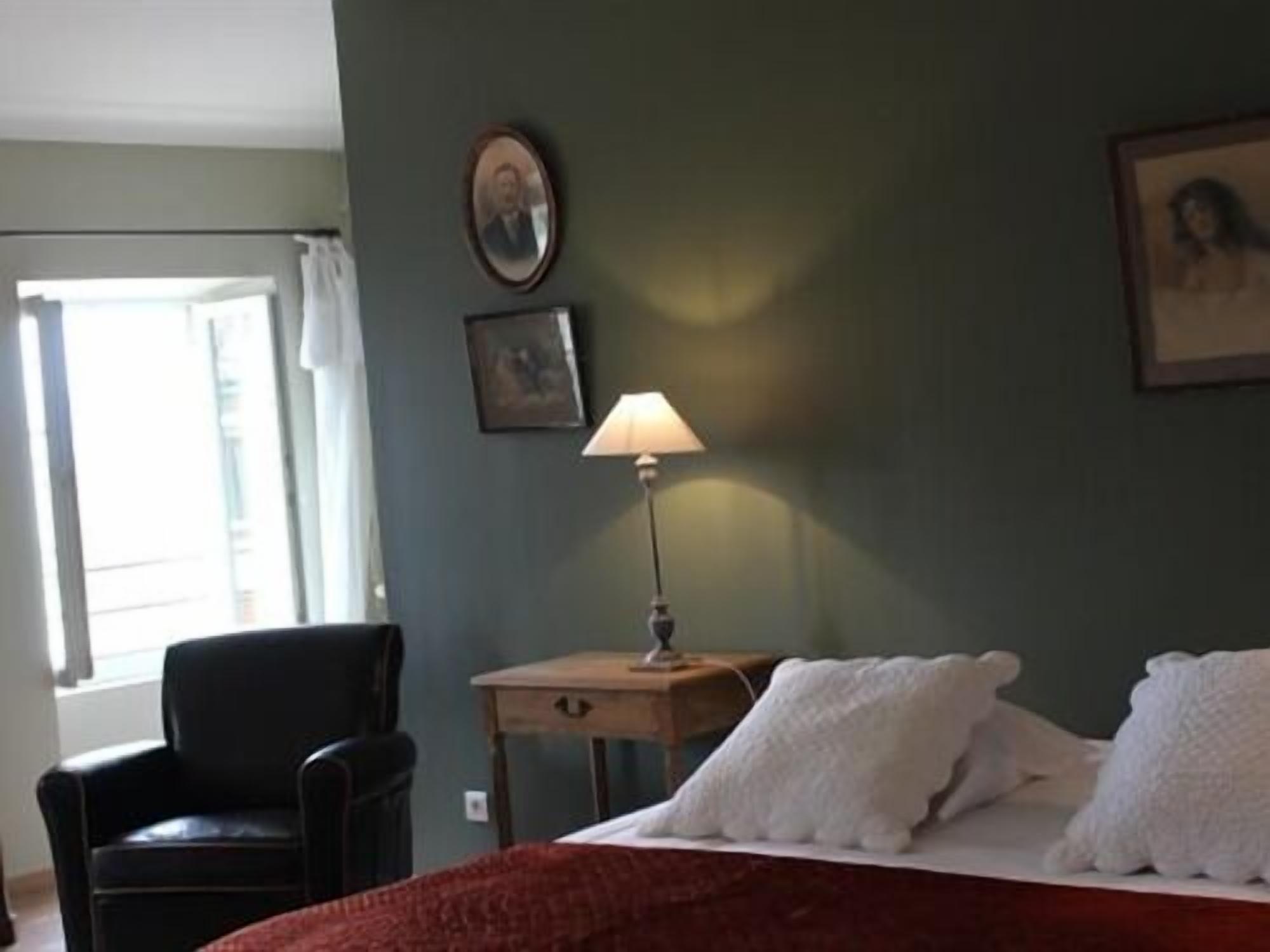 A bedroom with a bed, a chair, a nightstand with a lamp, and a window with curtains.
