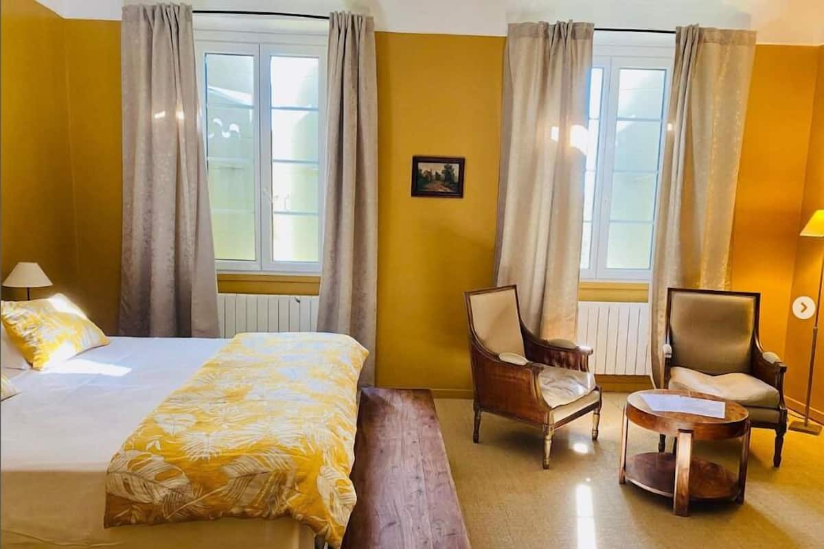 Une chambre d’hôtel avec un lit, deux fauteuils, une petite table et un banc.
