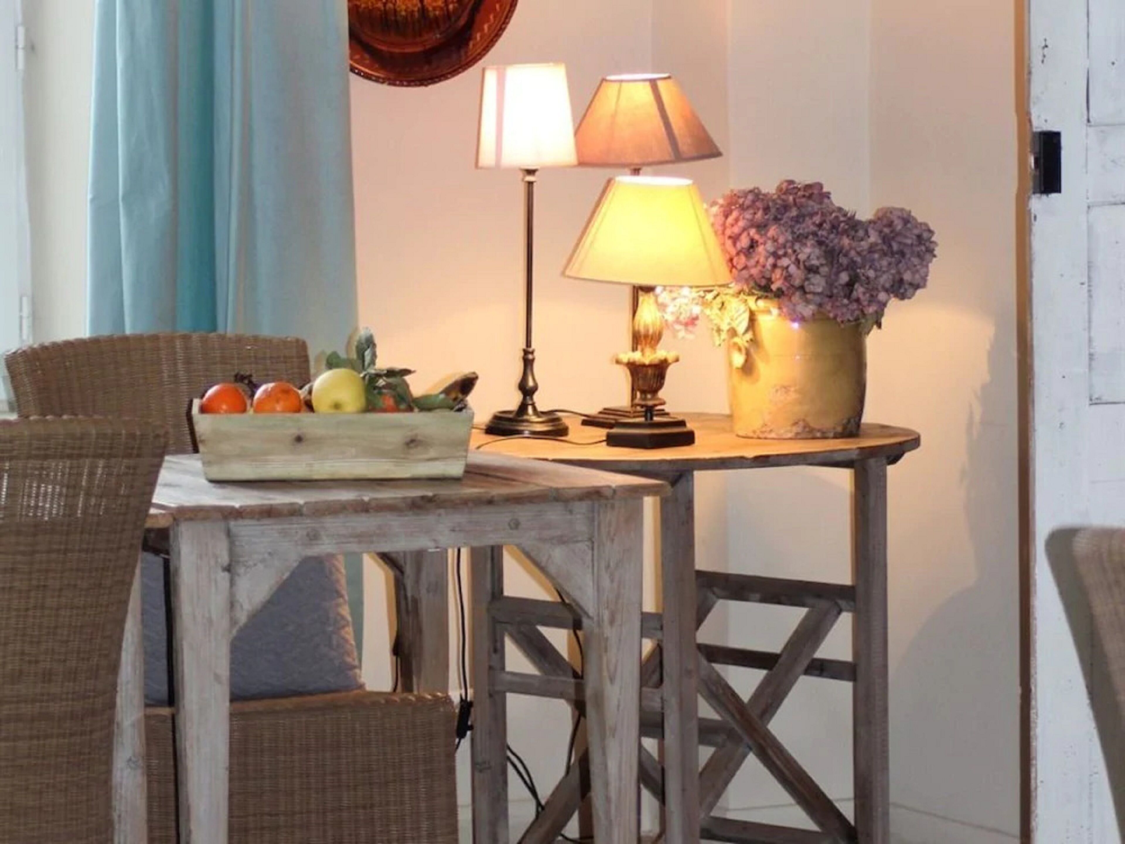 A rustic wooden table with a fruit basket, a lamp, and a vase with flowers.
