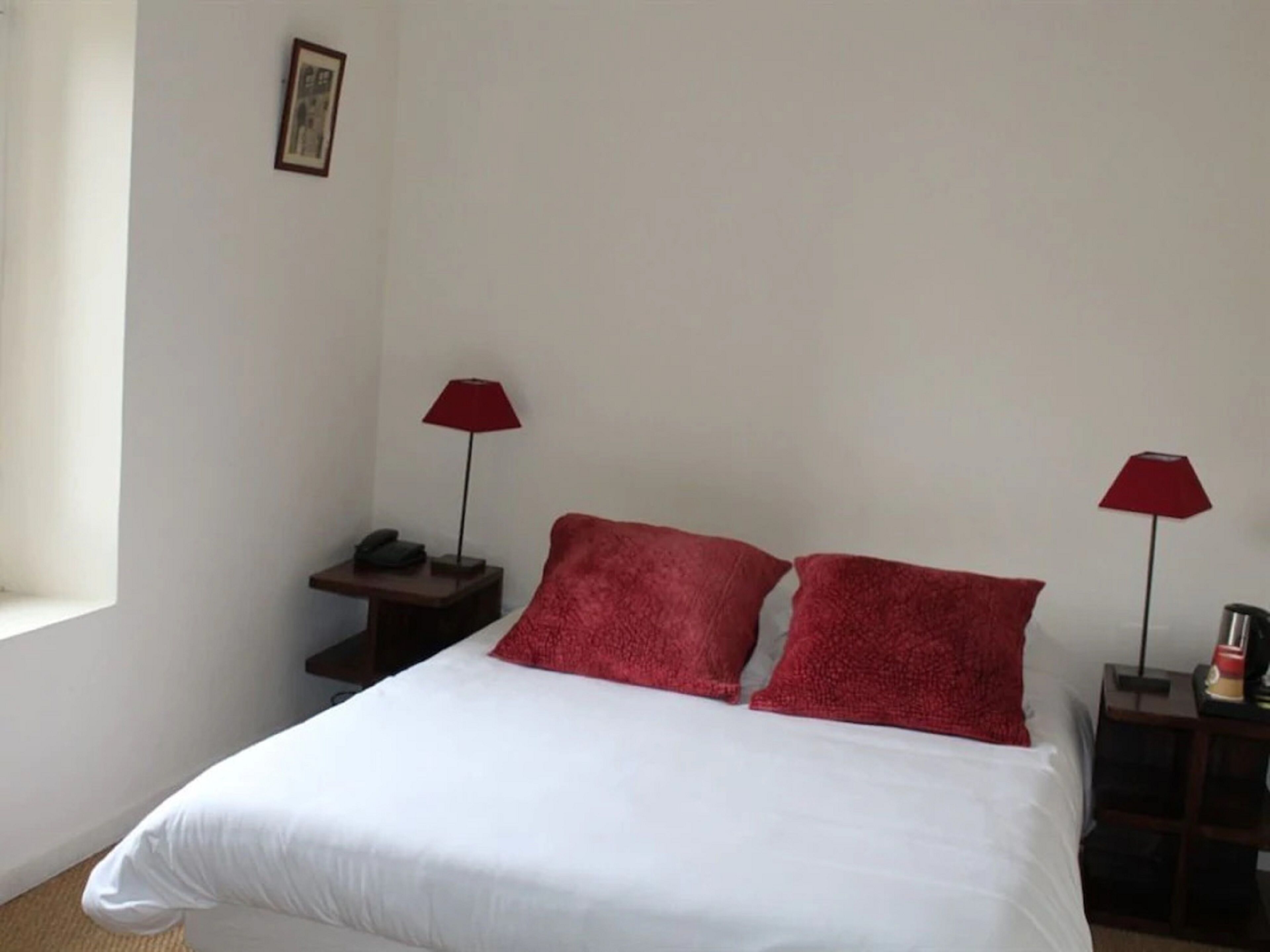 A simple, clean room with a bed, two red lamps, a nightstand, and a small table with a phone.