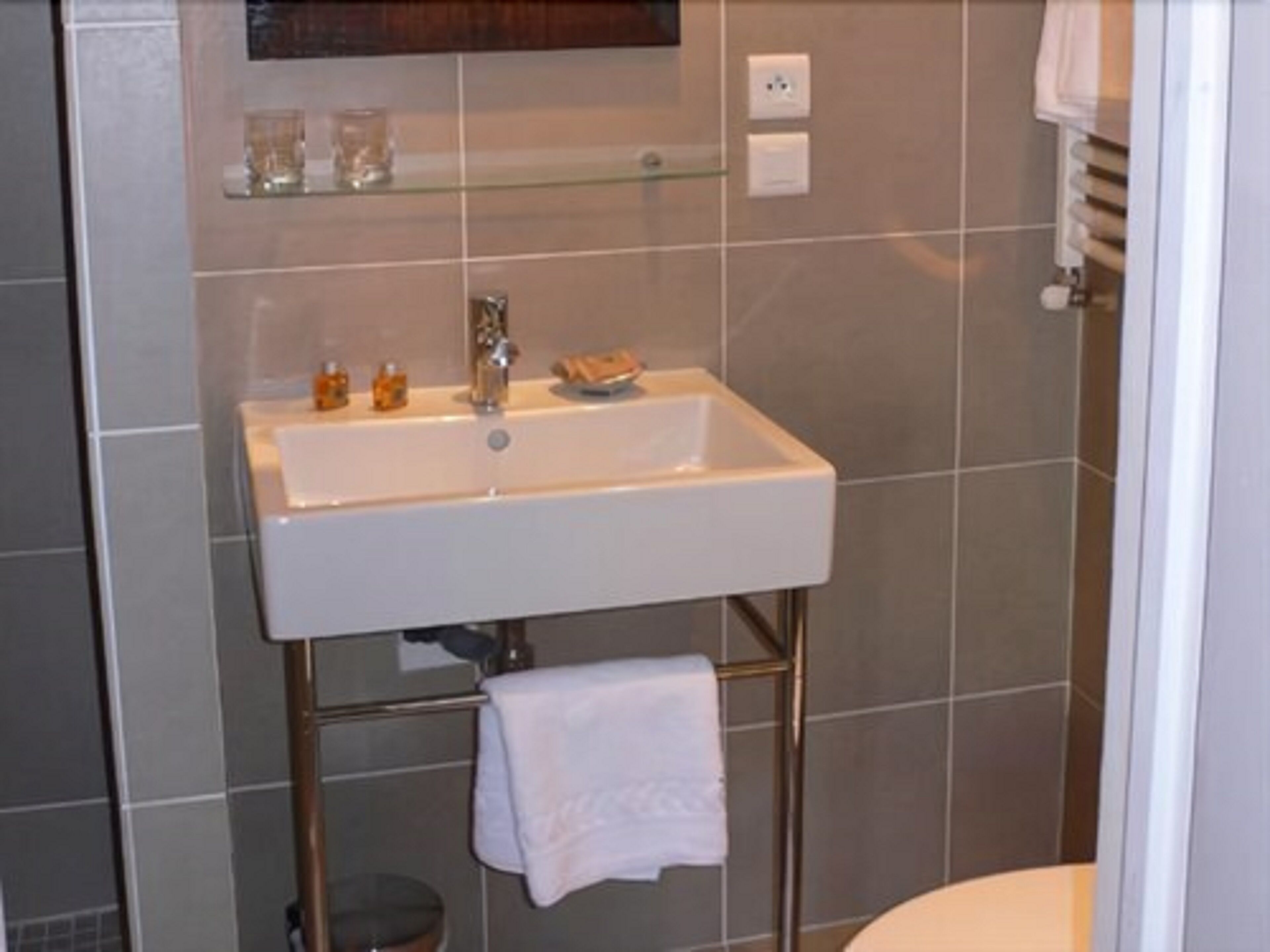 Une salle de bain avec un lavabo blanc, une étagère en verre au-dessus et une serviette suspendue à un porte-serviettes en métal.