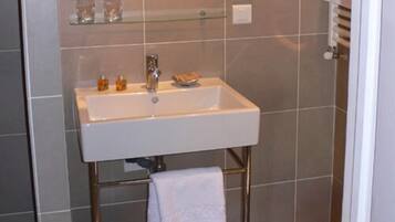 Une salle de bain avec un lavabo blanc, une étagère en verre au-dessus et une serviette suspendue à un porte-serviettes en métal.
