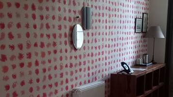 A hotel room with a bed, a desk, a mirror, and a radiator.