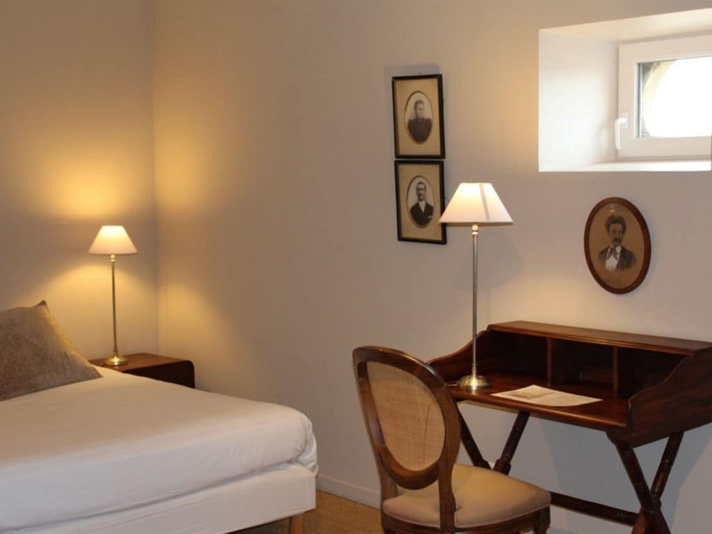 Habitación de hotel con cama, dos lámparas de noche, un escritorio con silla y cuadros en la pared.