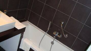 Un baño moderno con una bañera blanca, baldosas oscuras y un lavabo blanco.