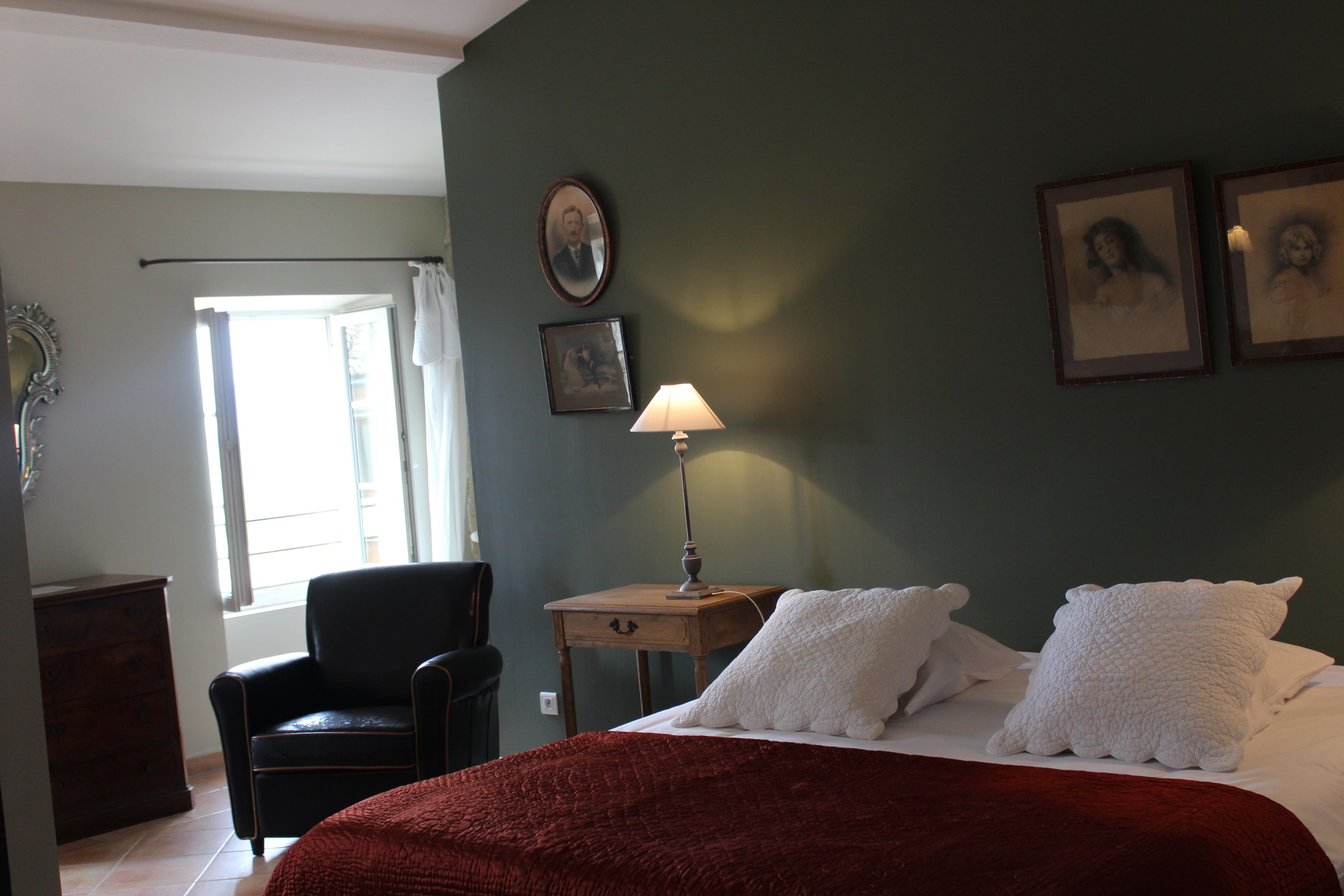 A bedroom with a bed, a chair, a nightstand with a lamp, and framed pictures on the wall.