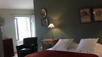 A bedroom with a bed, a chair, a nightstand with a lamp, and framed pictures on the wall.