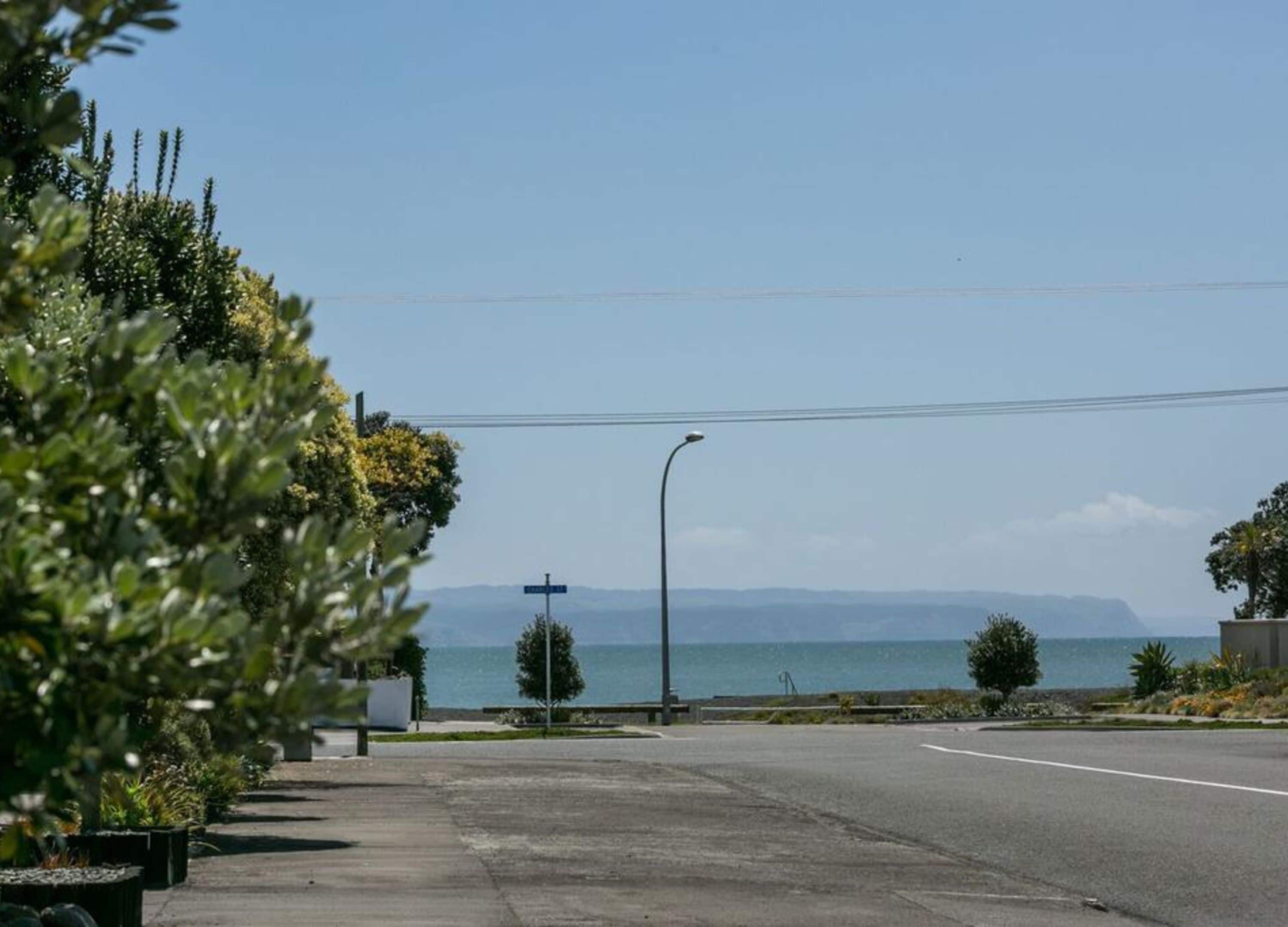 Une route côtière bordée d’un lampadaire et d’un panneau indicateur, entourée de verdure et offrant une vue sur la mer.