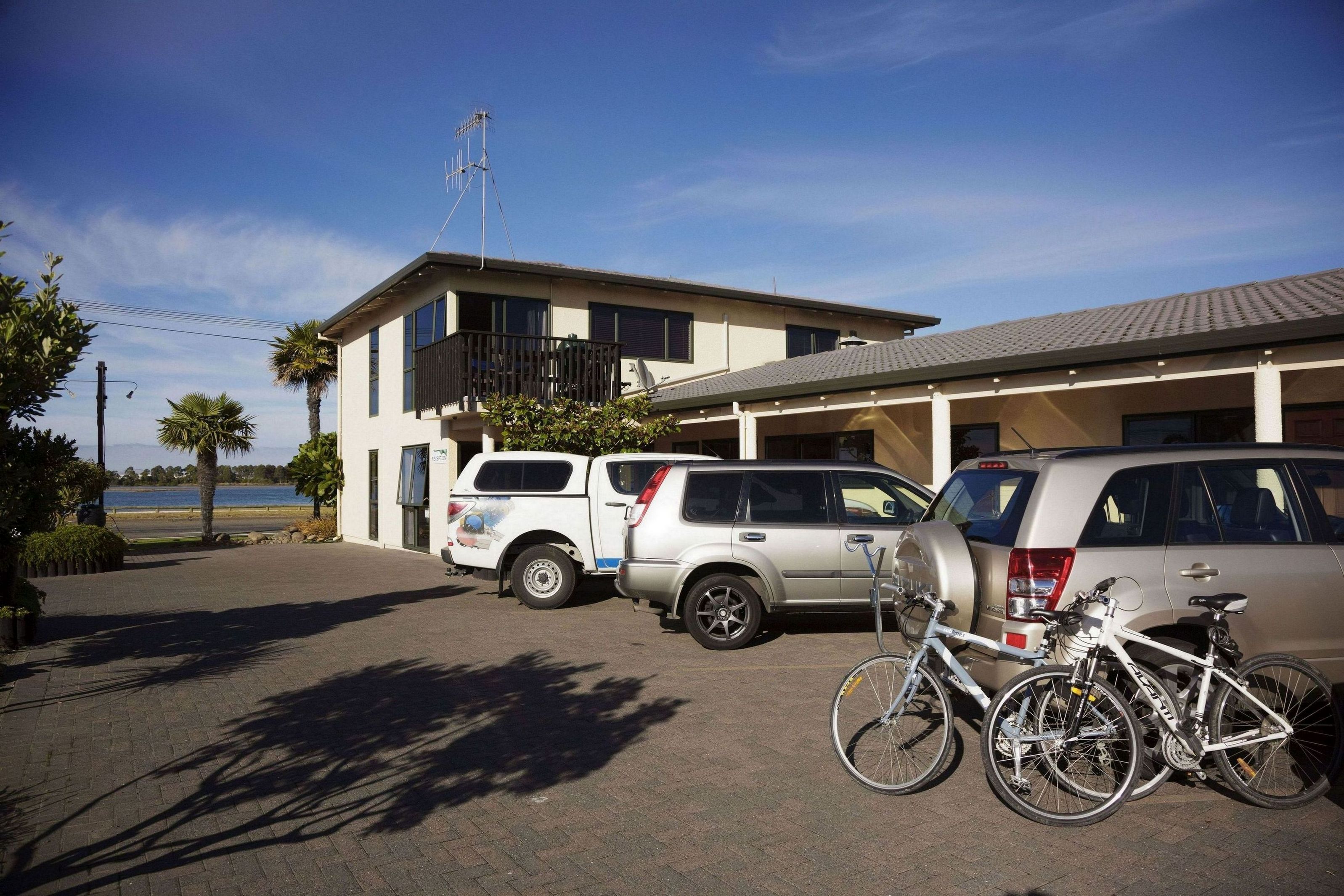 Un edificio con techo plano, un balcón y un estacionamiento con dos SUV y una bicicleta.