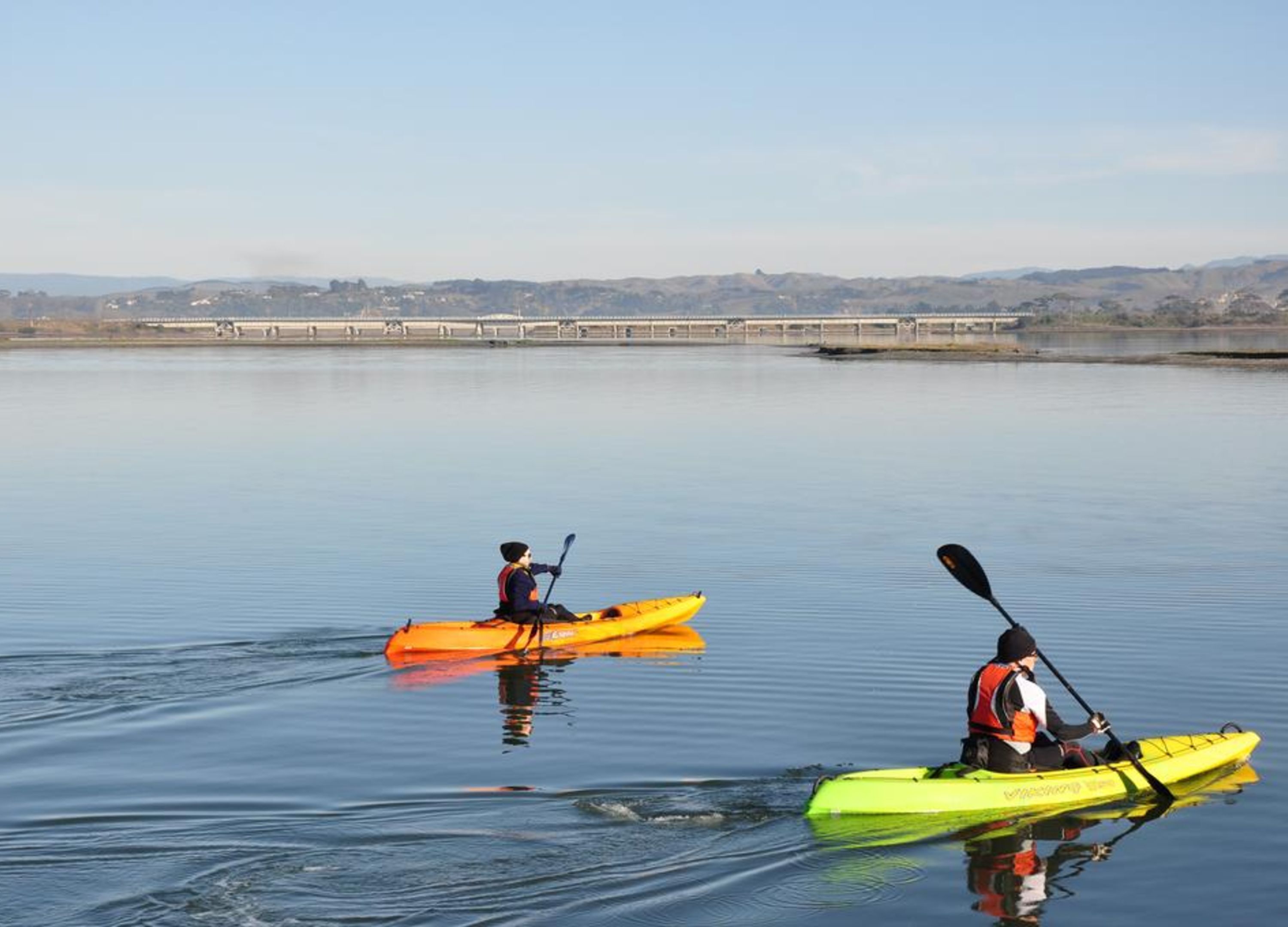 Two kayaks on calm water with a bridge in the background.
