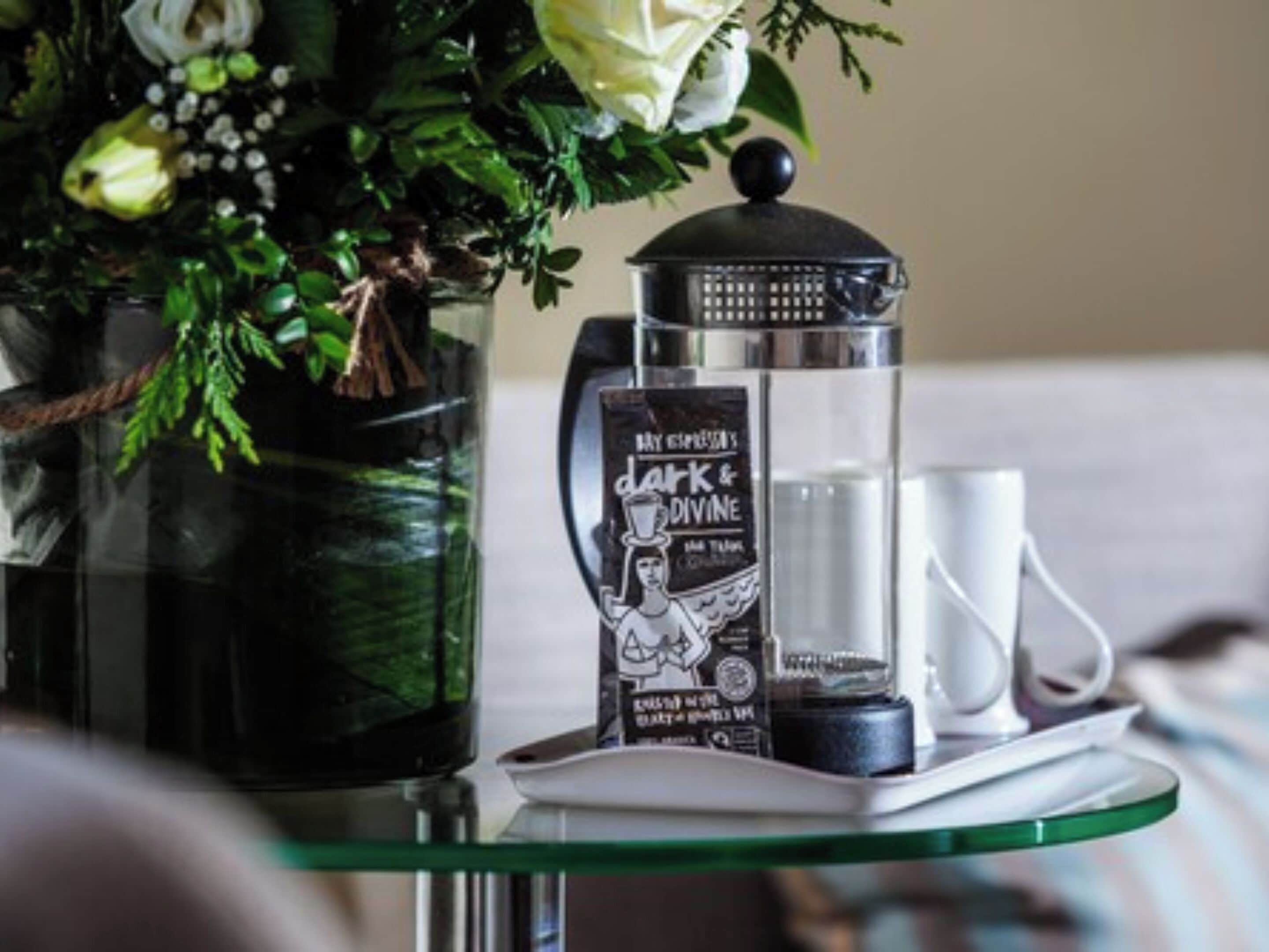 A tray with a coffee maker, a mug, and a decorative item on a glass table.