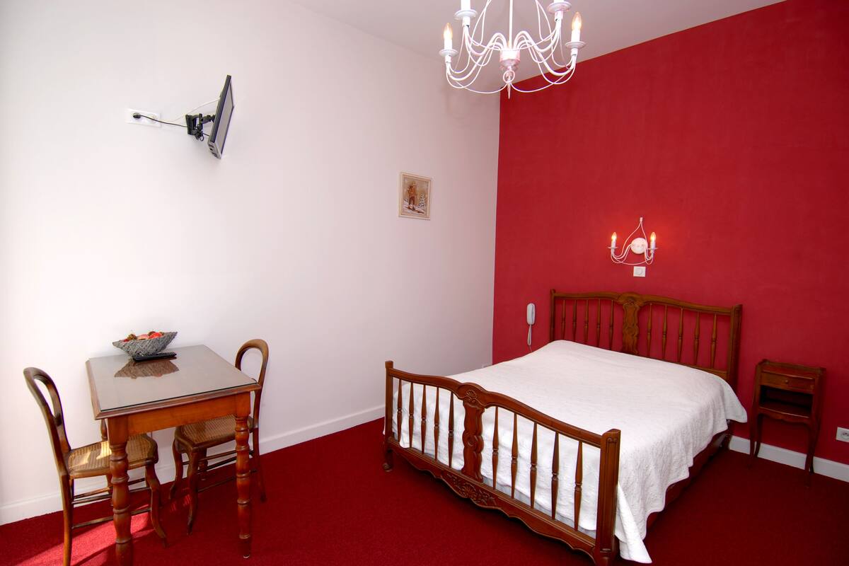 Une chambre à coucher avec un lit en bois, une table de chevet, une commode, un bureau avec une chaise et un lustre.