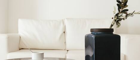 Une table ronde avec une tasse et une soucoupe blanches, un vase foncé avec une plante, et un canapé blanc en arrière-plan.