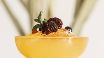 A cocktail in a yellow glass with a blackberry and orange garnish.