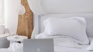 Una cama bien tendida con ropa de cama blanca, una computadora portátil y un par de lentes sobre la cama.