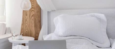 A neatly made bed with white bedding, a laptop, and a pair of glasses on the bed.
