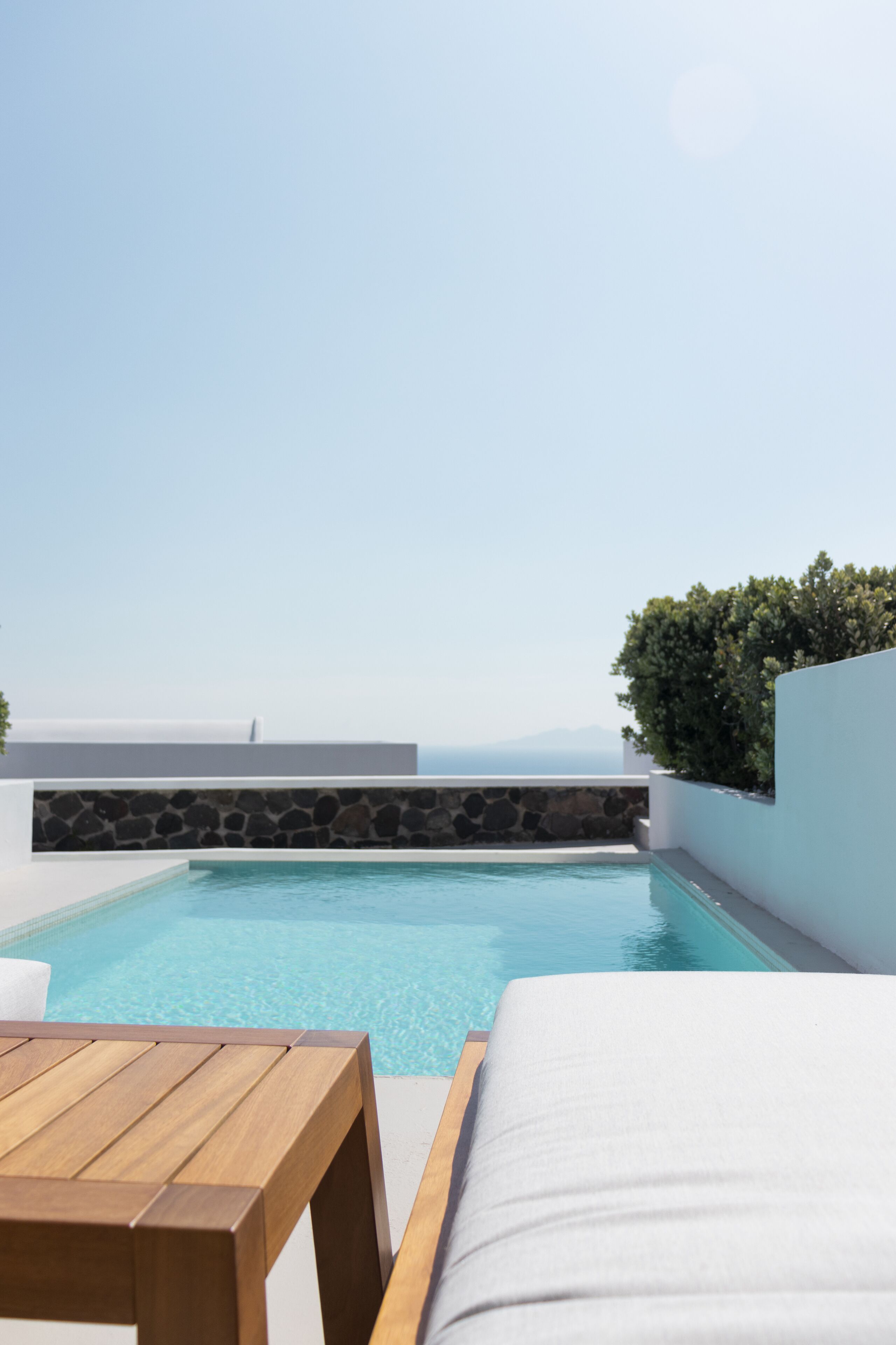 Piscina com muro de pedra e mesa de madeira em primeiro plano.