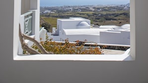 A view through an arched window overlooking a coastal landscape with white buildings and distant mountains.