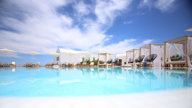 A pool area with lounge chairs and umbrellas, surrounded by white buildings with a clear blue sky above.