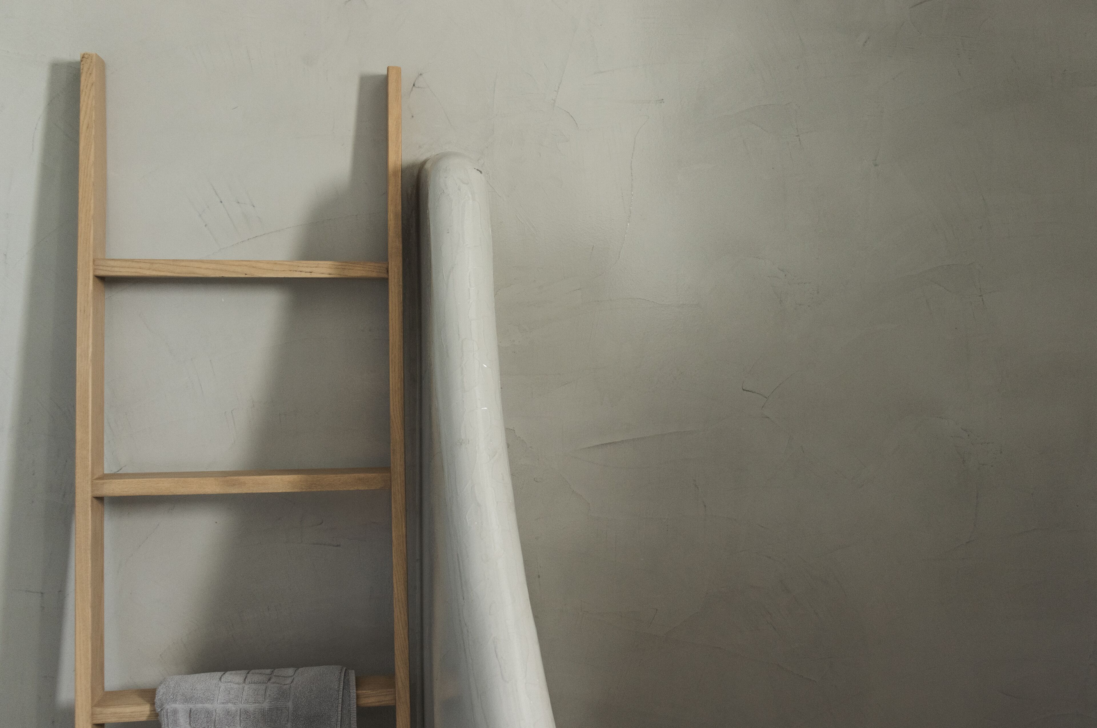 A wooden ladder leaning against a wall with a rolled-up white sheet.