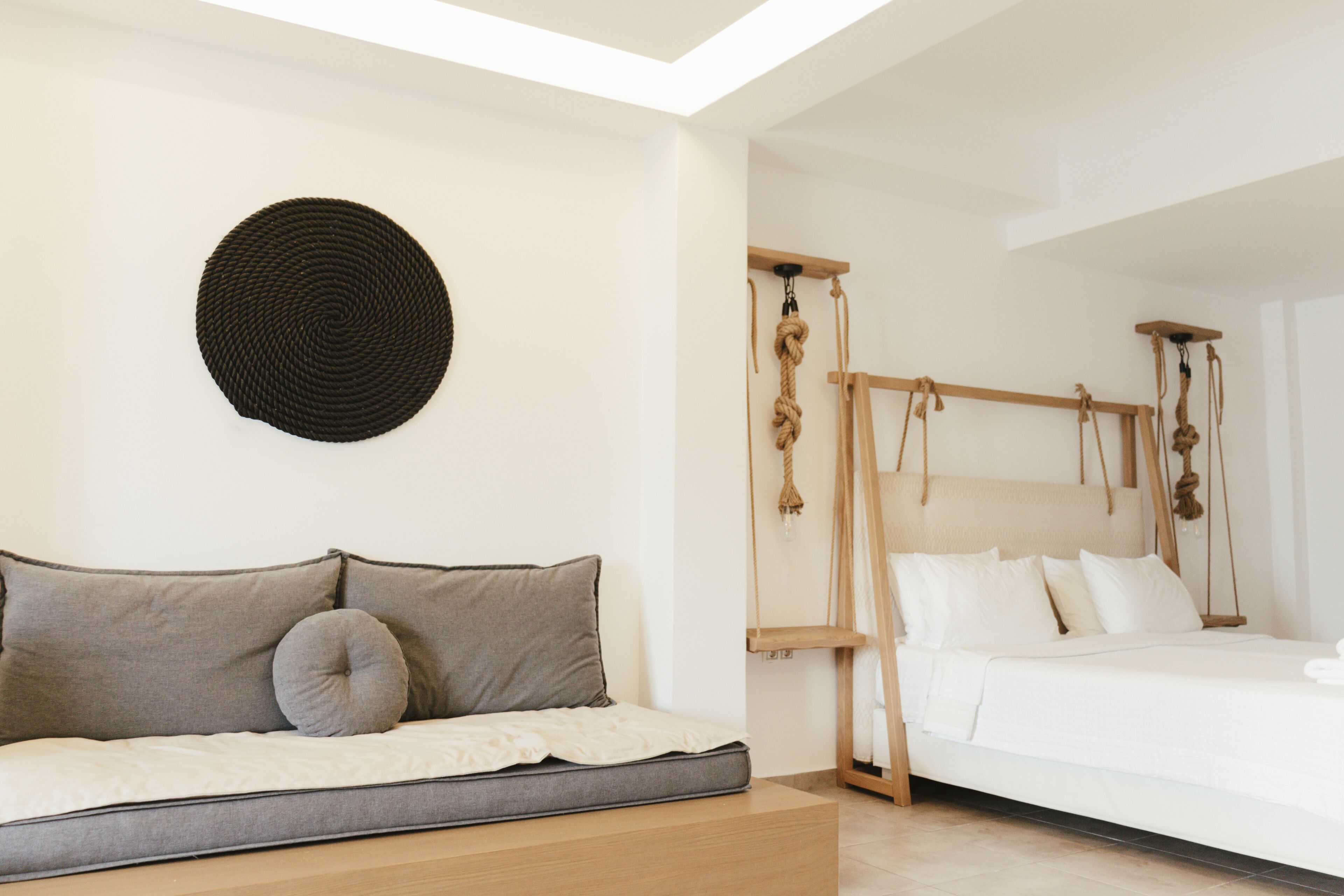 A modern bedroom with a sofa bed, a hanging swing bed, and a circular woven wall art piece.