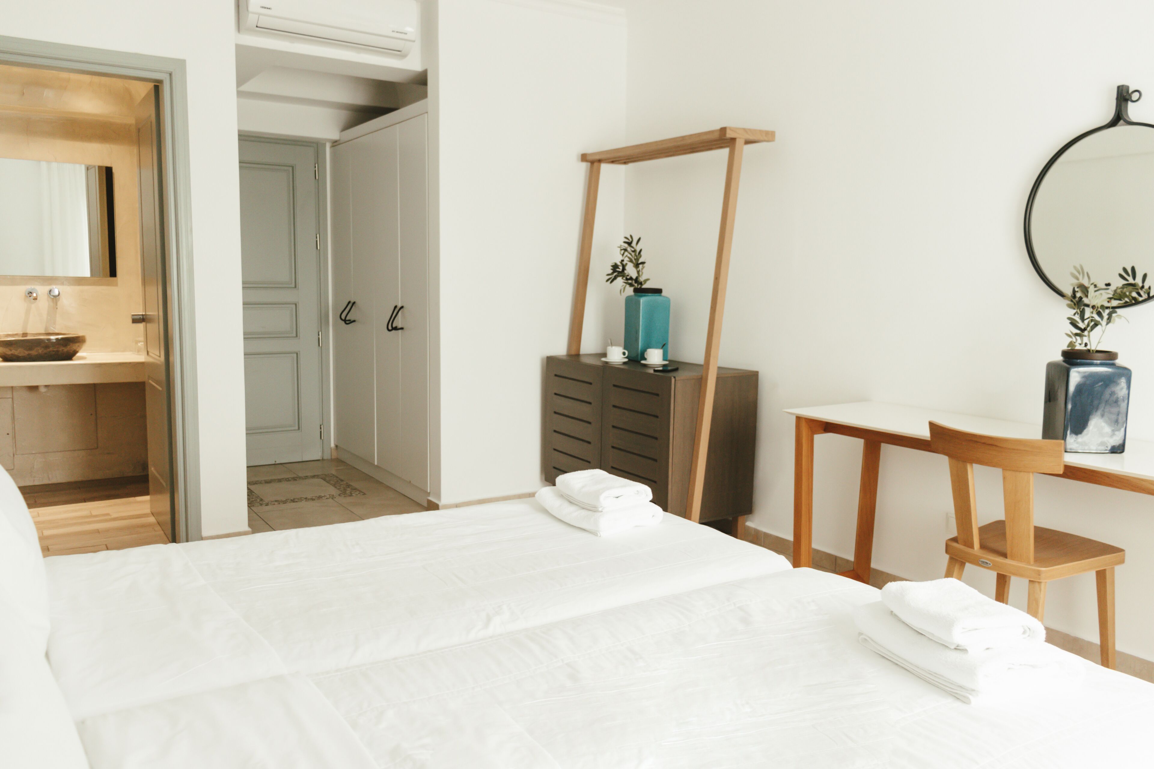 A hotel room with a bed, a wooden chair, a desk, a mirror, and a wardrobe.
