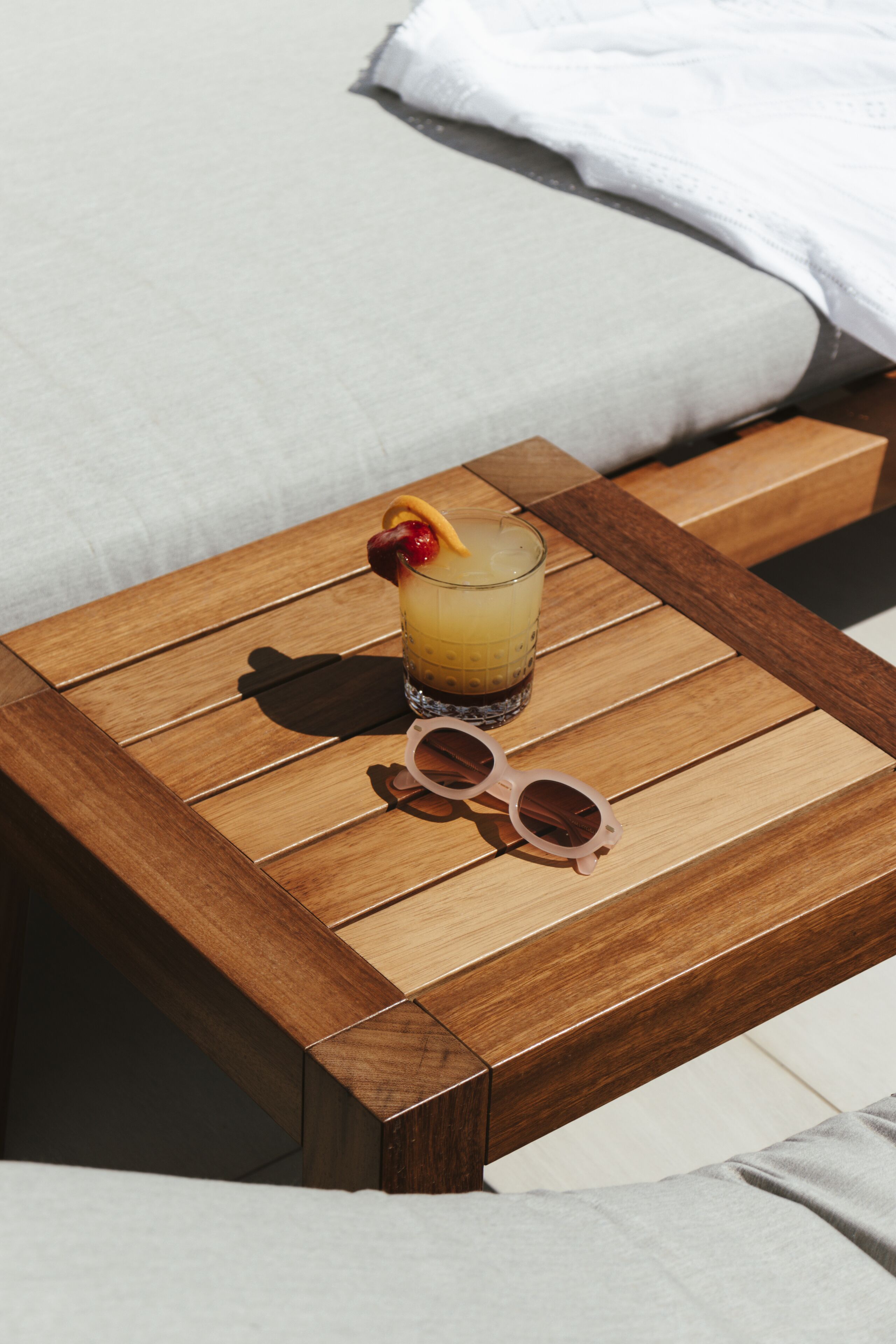 A wooden table with a drink and sunglasses on it.