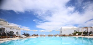 A poolside area with lounge chairs and umbrellas, a clear sky, and a pool. - Astro Palace Hotel & Spa (Santorini)