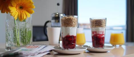 Une table de petit-déjeuner avec un vase de fleurs jaunes, deux verres contenant des couches de fruits et de céréales, et une machine à café en arrière-plan.