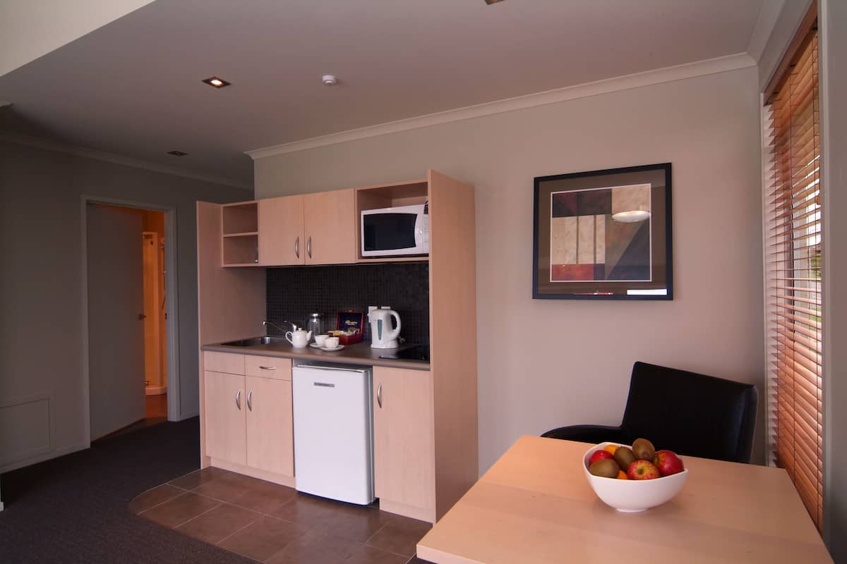 A compact kitchen with a microwave, kettle, and a bowl of fruit on the table.