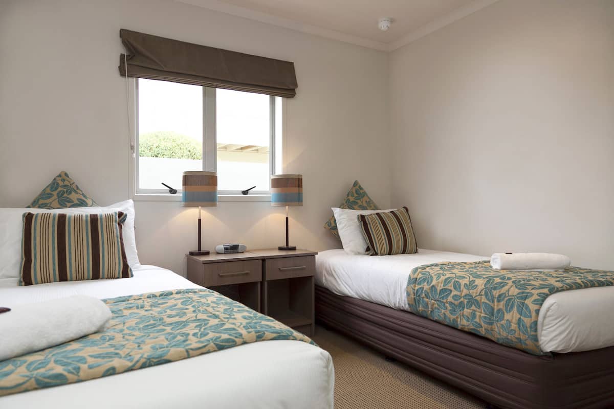 A hotel room with two beds, a window with a view, and a desk with a lamp.