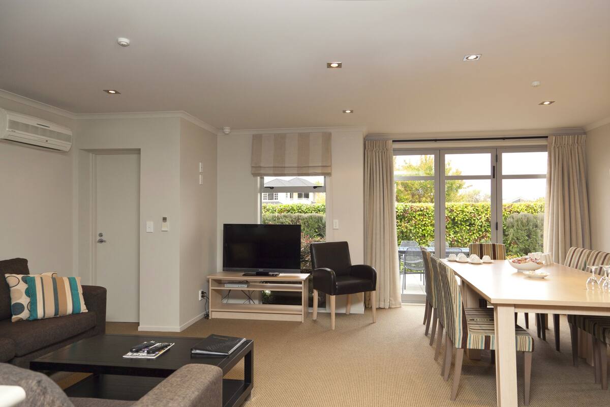 A modern living room with a flat-screen TV, a dining table with chairs, a sofa, and a coffee table.