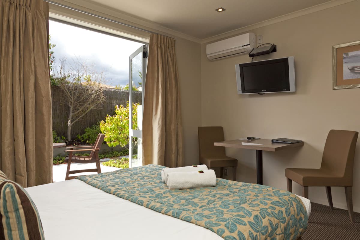 A hotel room with a bed, a desk, two chairs, a TV, and an air conditioning unit.