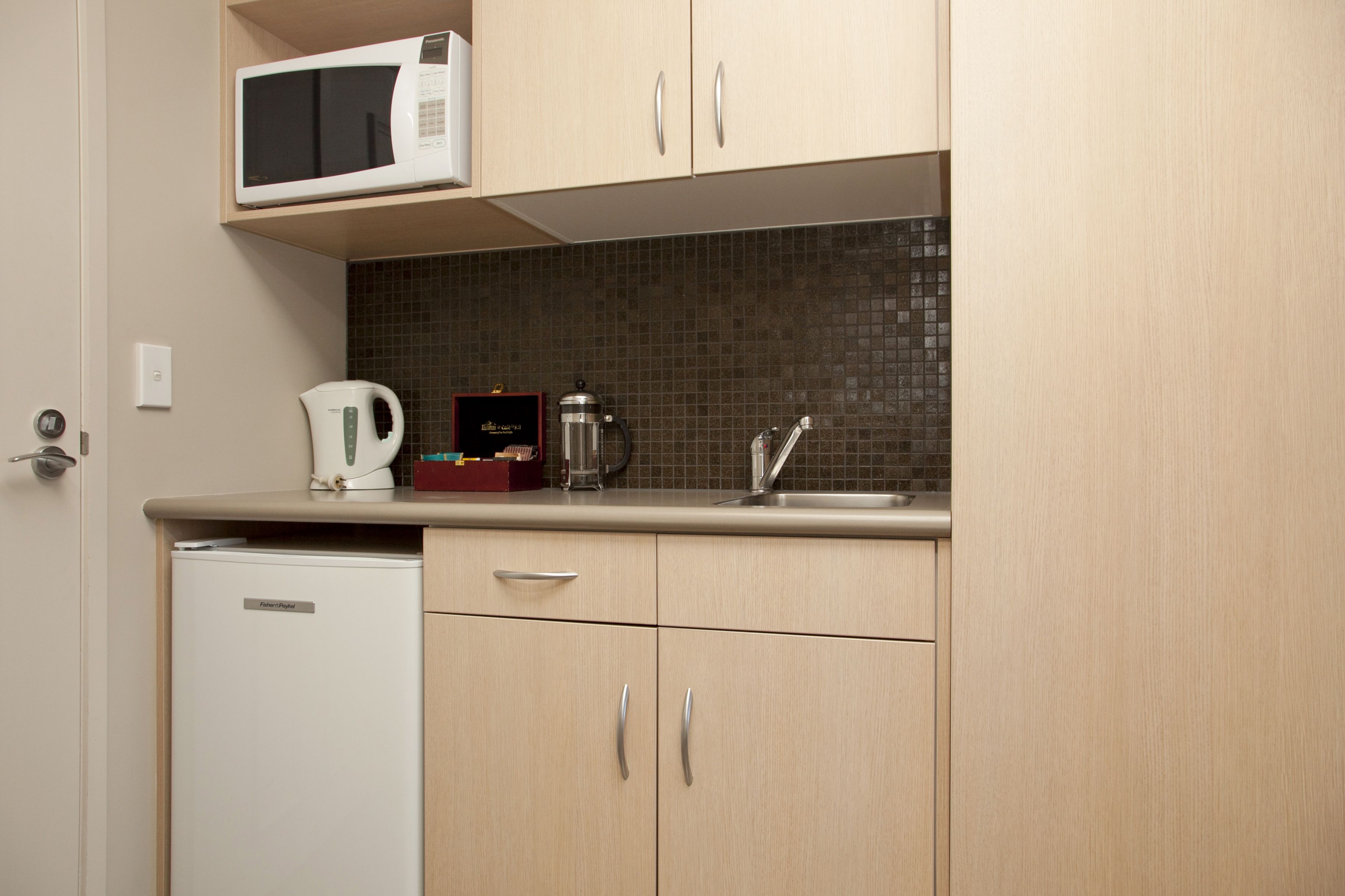 A compact kitchen with a microwave, kettle, and coffee maker on the counter, and a refrigerator.