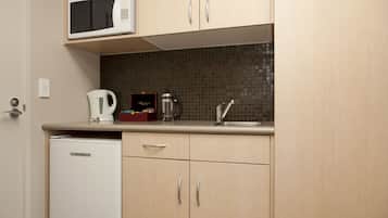 A compact kitchen with a microwave, kettle, and coffee maker on the counter, and a refrigerator.