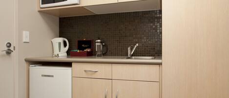 A compact kitchen with a microwave, kettle, and coffee maker on the counter, and a refrigerator.
