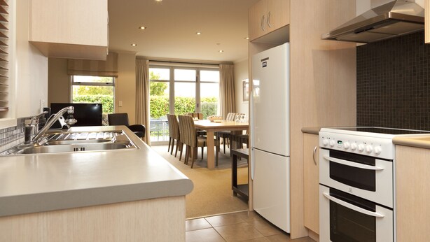A modern kitchen with a built-in oven, a refrigerator, and a dining area with a table and chairs. - Beechtree Motel (Taupo)