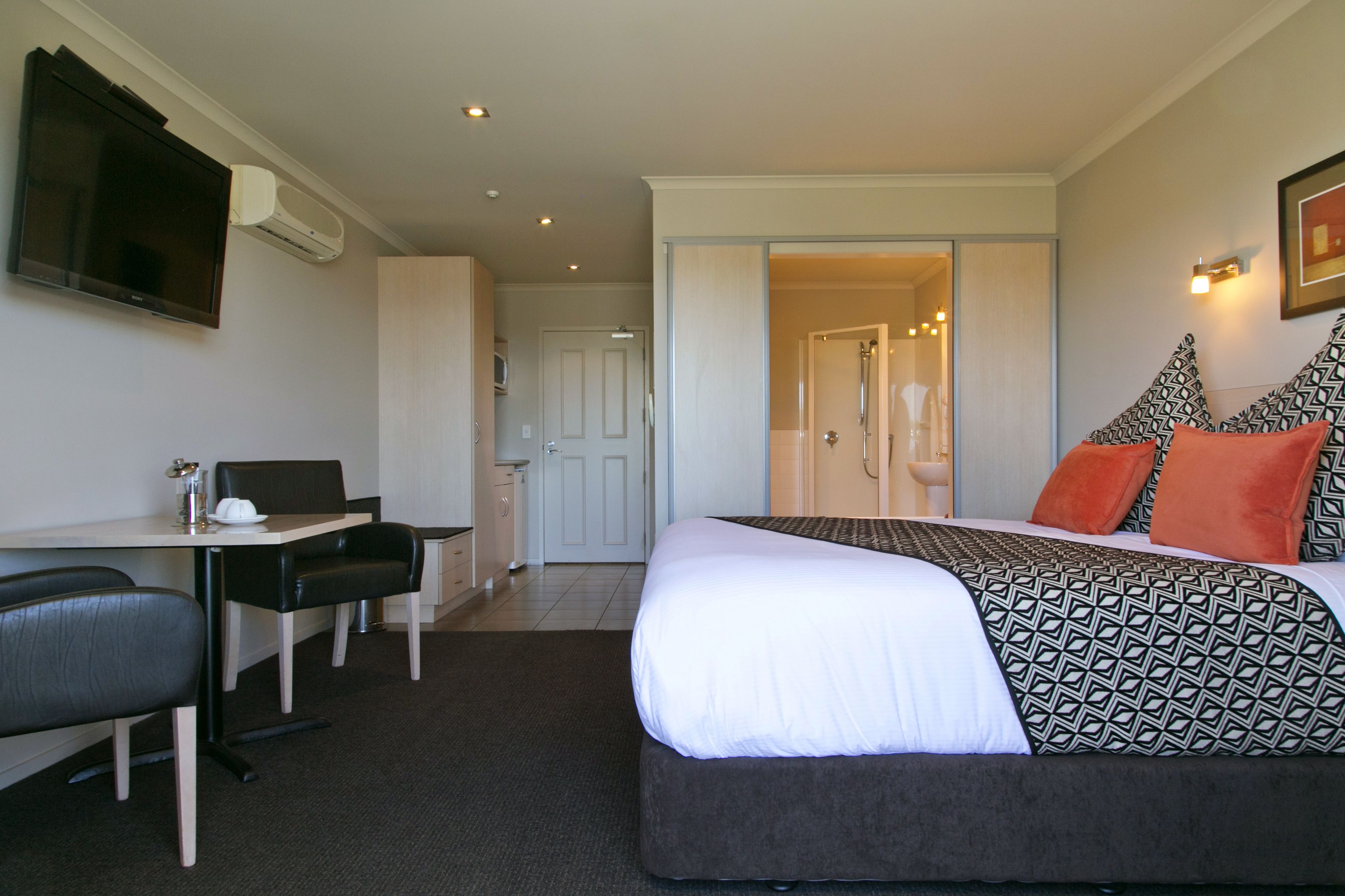 A hotel room with a bed, a desk with a chair, a television, and a bathroom visible through an open door.