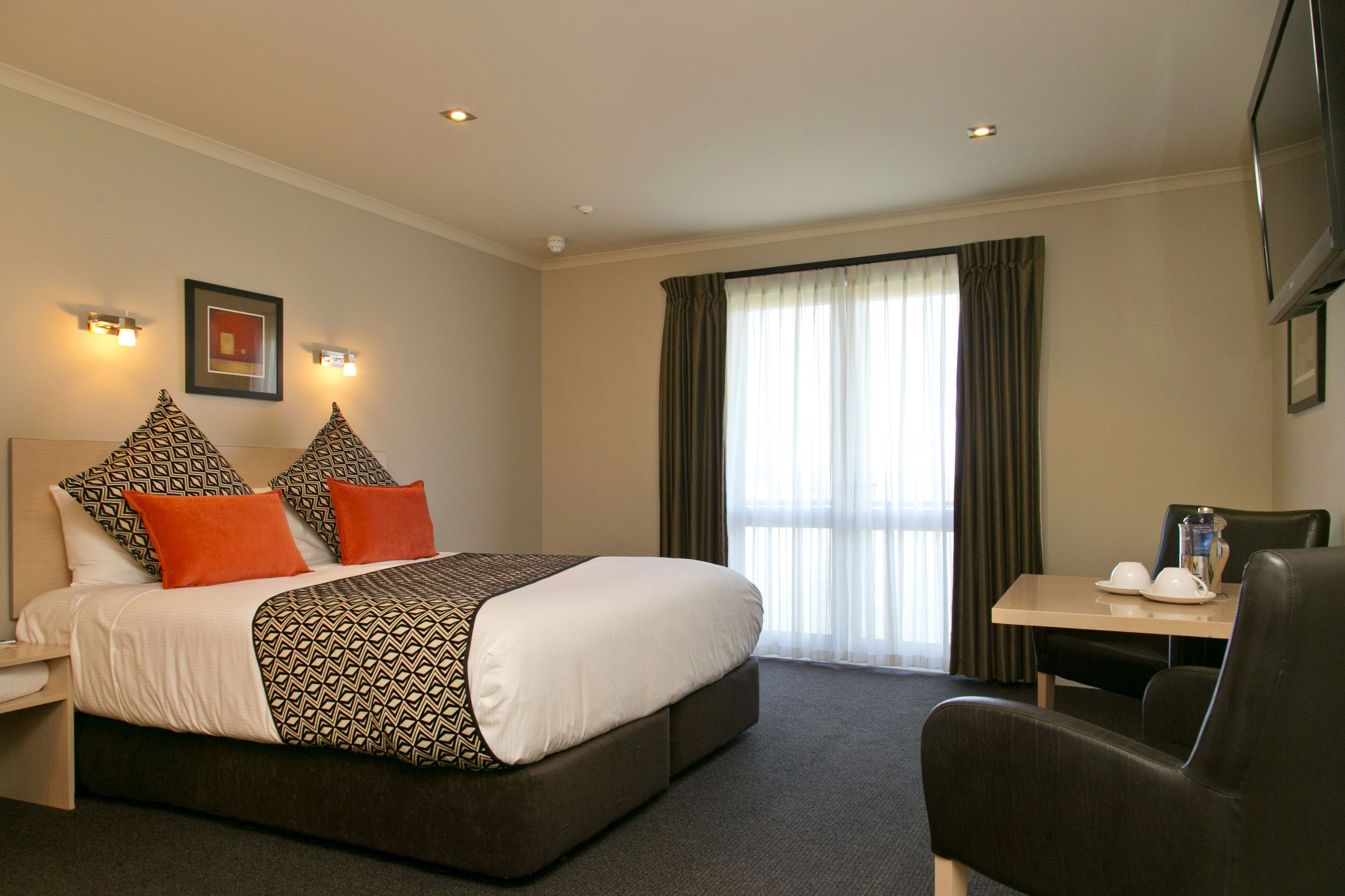 A hotel room with a large bed, a desk with a chair, and a television mounted on the wall.