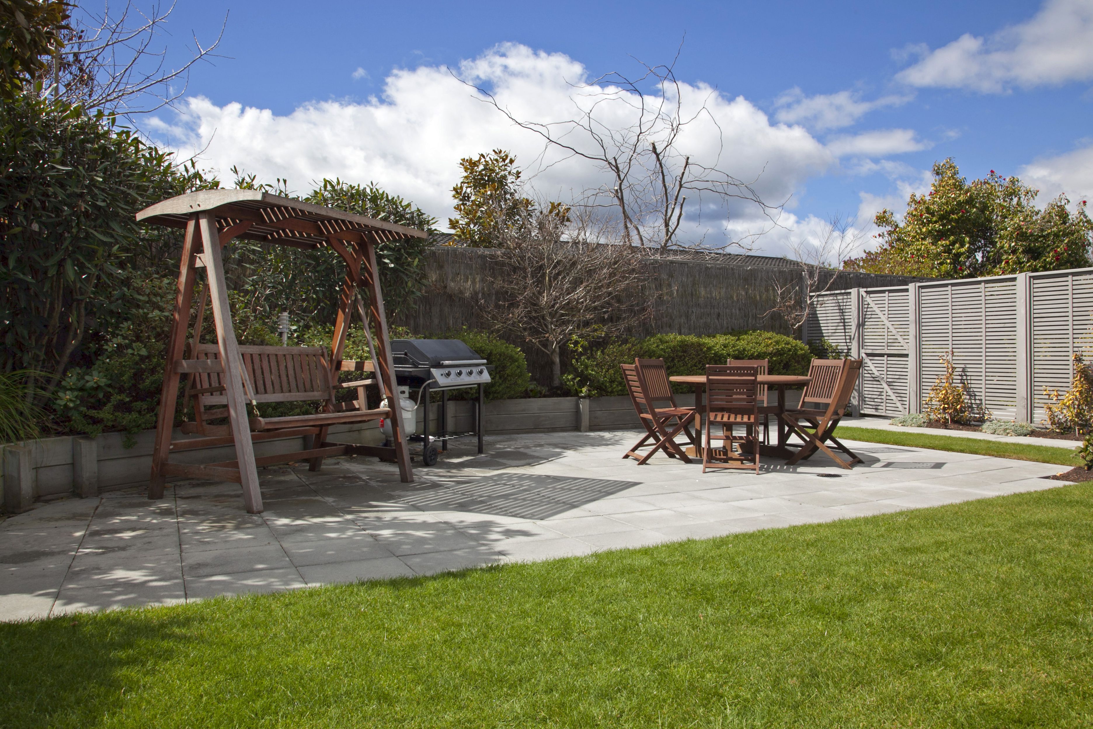 A patio with a swing set, a grill, and a dining table with chairs.